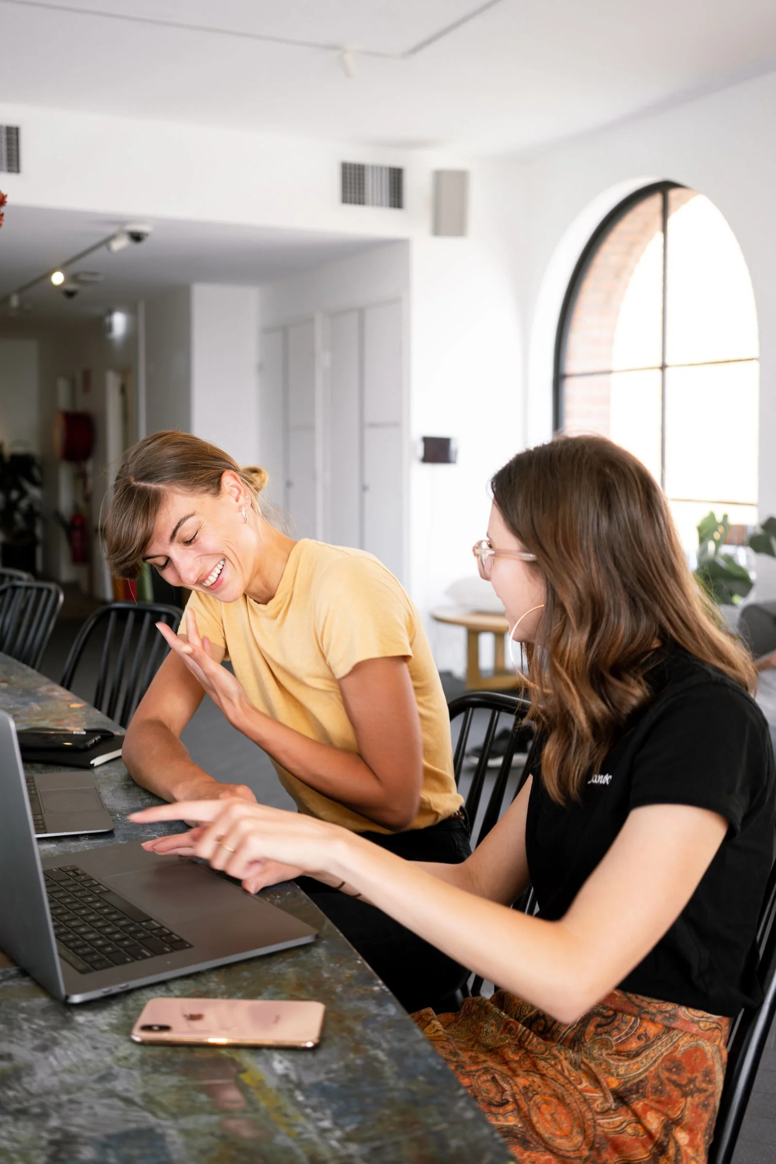 Deux jeunes femmes rient en travaillant ensemble devant un ordinateur portable